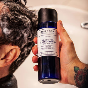 black tea  strengthening shampoo held by a barber above a clients head