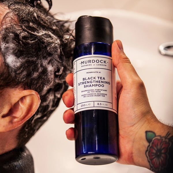 black tea  strengthening shampoo held by a barber above a clients head